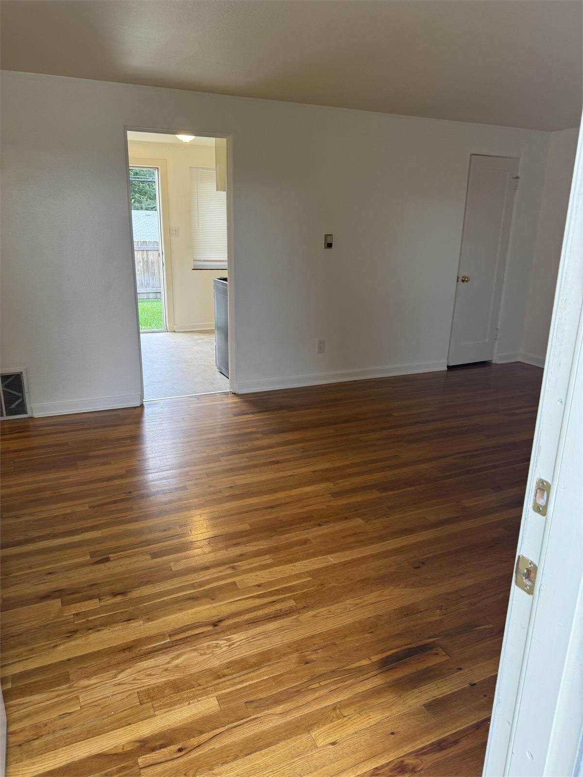 Second view of the living room with hardwood floors and an open doorway to the kitchen